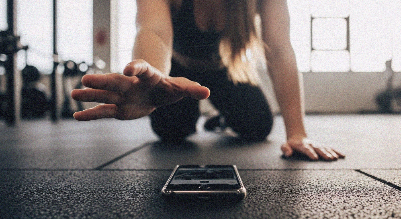 A woman in workout clothes reaches for her phone on the gym floor, illustrating the concept of documenting fitness routines for social media. - heatseekerproject.com